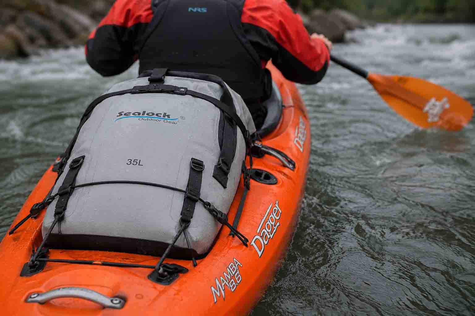 Field photography of a fully packed 35L TPU waterproof dry backpack with a tight 4-roll seal rigged flat on the stern deck of a Dagger Mamba 8.6 whitewater kayak